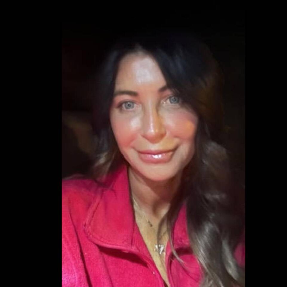 A woman with long dark hair wearing a red top smiles softly at the camera.