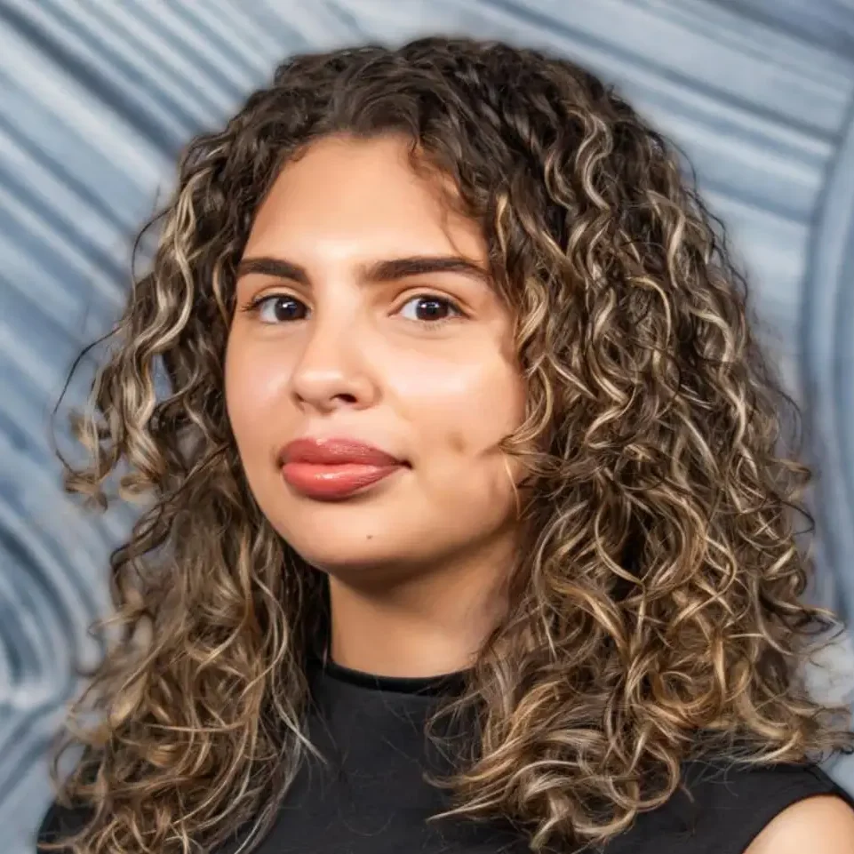 Young woman with curly hair and natural makeup looks confidently at the camera.