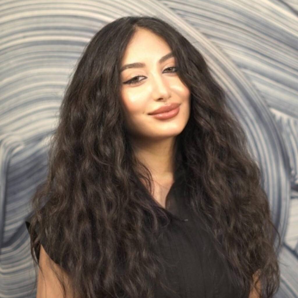 Woman with long curly hair smiling against a striped wall.